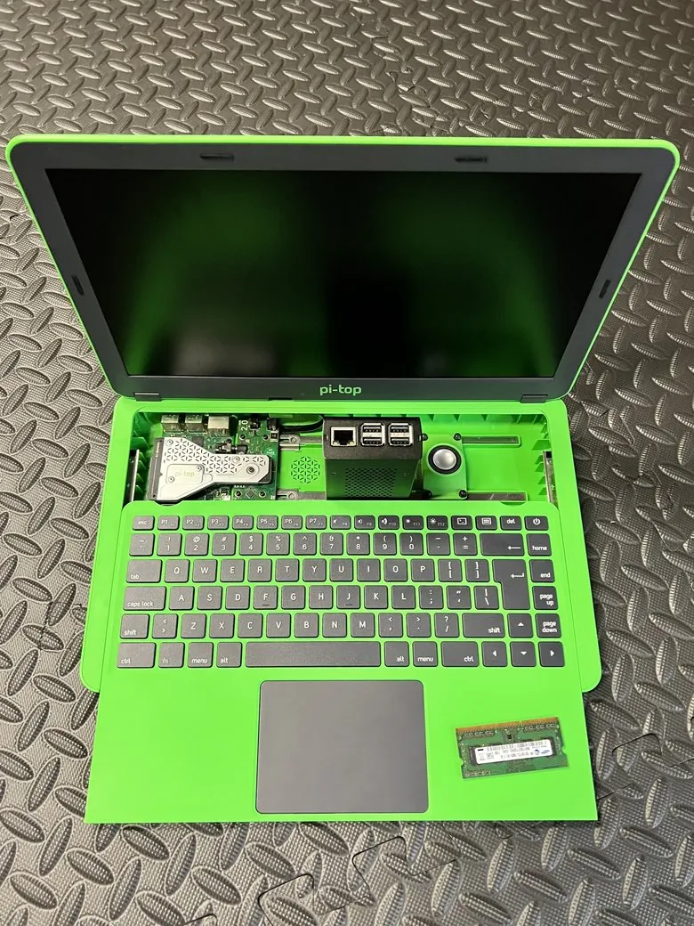 An open green pi-top modular laptop with the Raspberry Pi board, trackball, and internals exposed